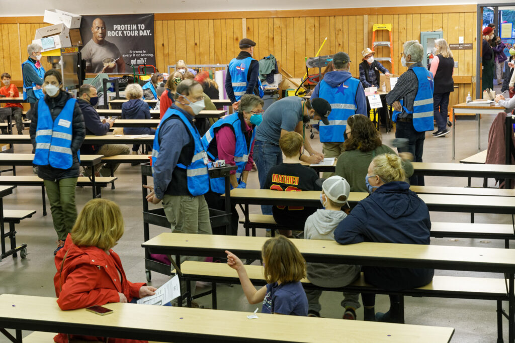 A school lunchroom with children and adults wearing blue vests as part of a COVID vacinnation day