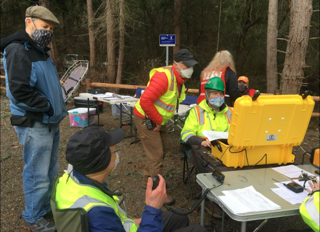 6 people in safety vests in the woods at outdoor tables with radio equipment